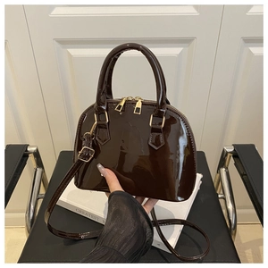 Detailed top view of dark brown patent leather shell bag with gold hardware on white book