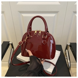 Detail of dark red patent leather shell bag with gold zipper and glossy finish