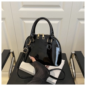 Close-up of a glossy black shell bag on a chair with gold hardware and mesh gloves