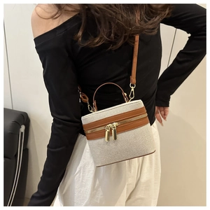 Detail of beige canvas and brown leather bucket bag with gold zippers and strap