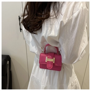 Close-up of bright pink mini crossbody bag with gold buckle and chain strap shown on model