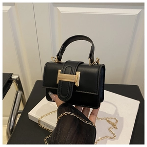 Close-up of black mini square handbag featuring a gold H-shaped buckle and chain strap