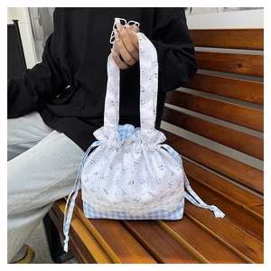 Floral and checkered drawstring lunch bag with lace detail held on wooden bench