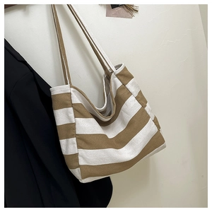 Detail of khaki striped canvas tote bag hanging on wooden hanger with black coat