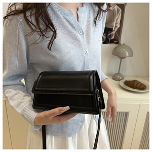 Close-up of black rectangular crossbody bag with fold-over flap and stitched detailing