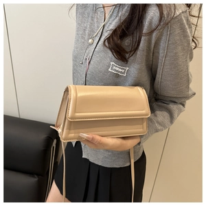 Detail view of the beige small square bag featuring a flap closure and smooth texture