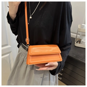 Detail of an orange textured leather crossbody bag with adjustable strap and gold hardware