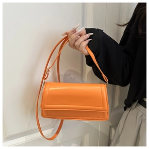 Detail view of orange rectangular crossbody bag with adjustable strap and flap closure