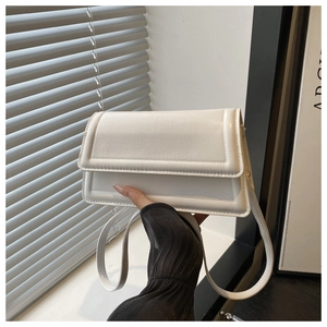 Detail of white rectangular flap crossbody bag showing textured synthetic leather and stitching