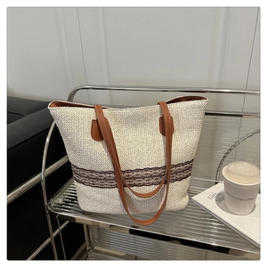 Detail of woven tote bag with brown leather handles on a silver metal cart