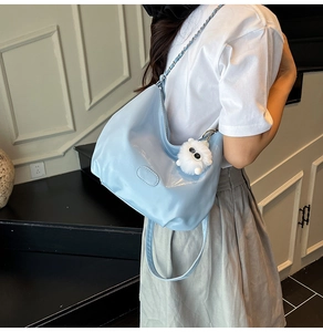 Detail of light blue hobo bag with glossy finish, chain strap and white plush pompom charm