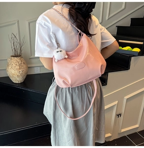 Detail of pink patent leather hobo bag with glossy finish and white plush charm on strap
