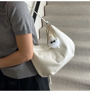 Weiße Halbmond-Tasche mit Plüsch-Anhänger getragen von einem Model auf der Treppe