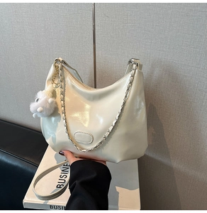 Detail der cremeweißen Lackleder-Halbmondtasche mit Silberkette und Plüsch-Anhänger