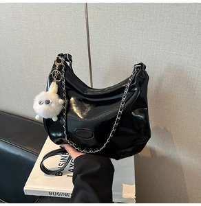Detail view of glossy black crescent tote bag with eye-design plush pendant and chain