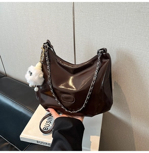 Detail of dark brown patent leather hobo bag with silver chain and plush charm