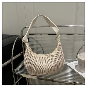 Detailed close-up of woven hobo bag with knotted strap and metal zipper on glass stand