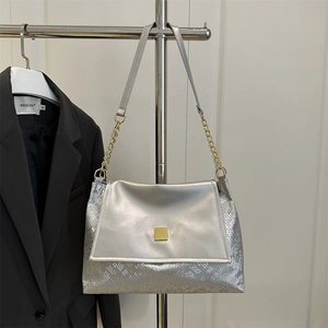 Sac à bandoulière argenté avec motif serpent et chaîne dorée exposé sur un portant