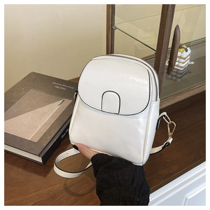Detail of white leather phone bag with gold hardware and zipper on a dark wood table