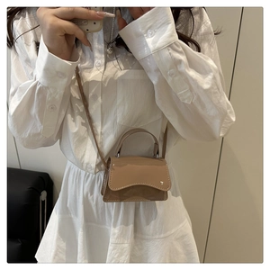 Close-up of khaki micro square bag with curved flap and top handle worn by a model