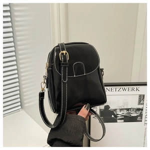 Detail of glossy black patent leather phone bag with white contrast stitching and gold hardware