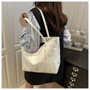 Detail of white tote bag with colorful wavy embroidery and embossed letters on handle strap