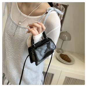 Detail einer schwarzen Lackleder-Mini-Handtasche mit schmalem Gurt für elegantes Tragen