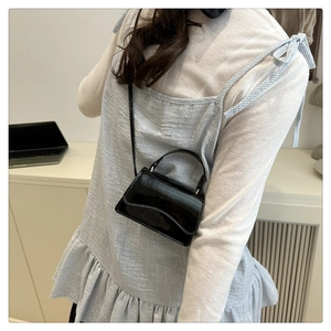 Glossy black patent leather mini crossbody bag shown with handle and thin strap on a model