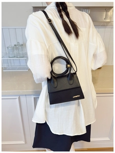 Détail d'un mini sac en cuir noir avec poignée circulaire et logo doré sur le côté