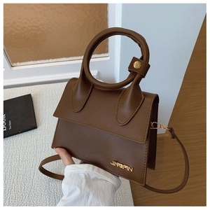 Détail d'un sac à main trapèze marron foncé avec grande poignée ronde et logo en métal