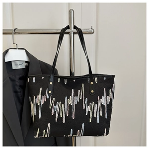 Detail of colorful embroidered wave pattern and gold rivet accents on a black tote bag