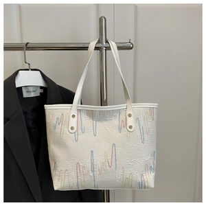 Detail of white tote bag featuring colorful wavy embroidery and gold rivet hardware