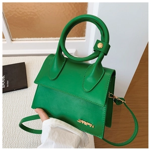 Détail d'un sac à main en cuir vert vif avec une poignée ronde et un logo en métal doré