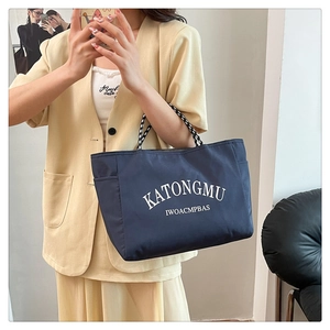 Detail of dark blue nylon tote bag with white lettering and checkered woven handles