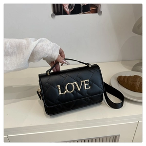 Detailed view of black quilted cylinder bag with golden LOVE letters and wide strap