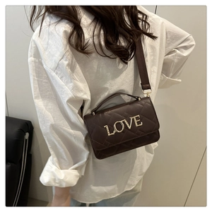 Detail of dark brown quilted cylinder bag with gold LOVE lettering and adjustable strap
