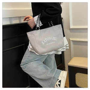 Detailed view of gray canvas tote bag with letter print and woven handles on a model
