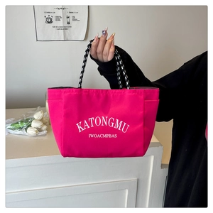 Detail of rose red tote bag featuring braided rope handles and white letter print