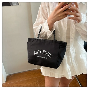 Close-up of a black tote bag with white lettering and striped straps in daily use