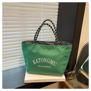 Close-up of green tote bag featuring striped rope handles and side pocket detail