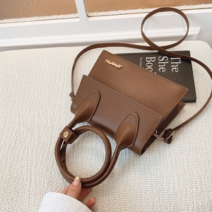 Sac bandoulière en cuir marron avec poignée ronde et logo en métal sur fond blanc