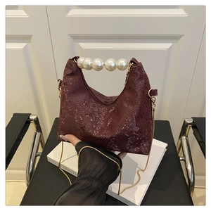 Detail view of burgundy snake pattern handbag with faux pearl handle and gold chain