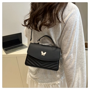 Détail d'un sac à bandoulière noir matelassé avec un charm papillon et boucles dorées