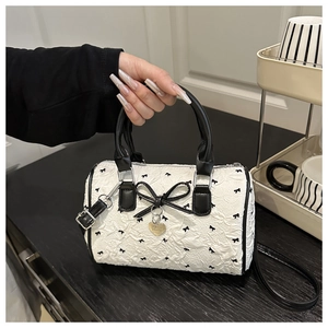 Detail of white seersucker Boston bag with black bows and heart-shaped metal tag