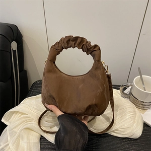 Dark brown pleated cloud hobo bag with top handle and shoulder strap in a cozy indoor setting
