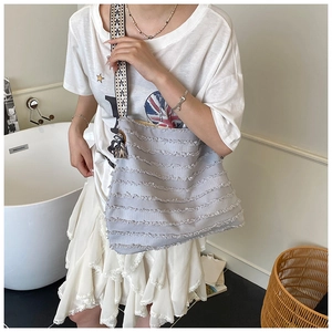 Détail du sac en toile gris clair avec volants effilochés et bandoulière géométrique