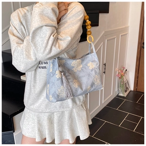Detail view of blue floral tote with wooden bead strap and tassel charm detail