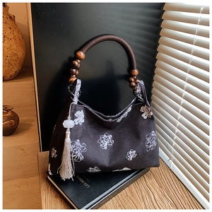 Detail of dark canvas tote bag featuring wooden bead handle and floral print on a book
