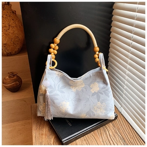 Detail of light blue floral tote bag with yellow wooden beads and gray tassel accent