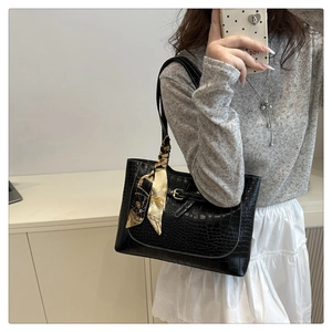 Close-up of black crocodile-textured tote bag with decorative silk scarf and gold buckle detail